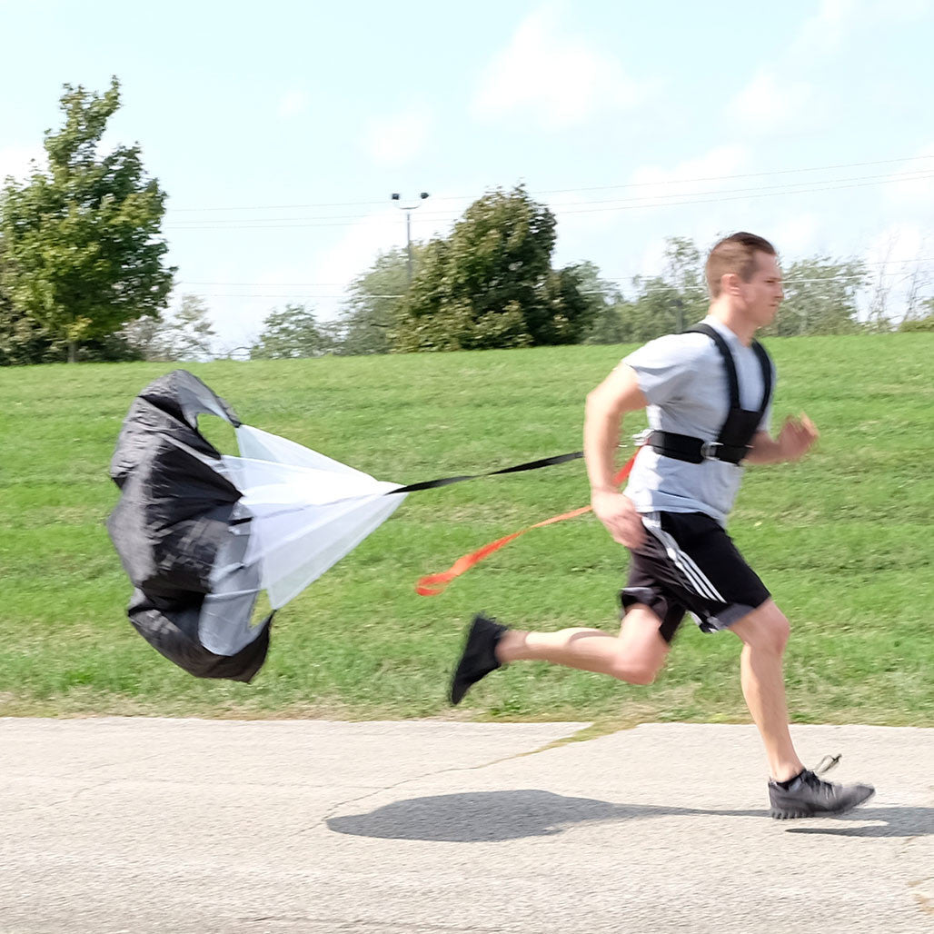 Athlete sprinting outdoors with Body-Solid BSTSH sled harness connected to a resistance parachute