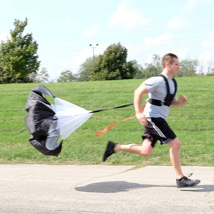 Athlete sprinting outdoors with Body-Solid BSTSH sled harness connected to a resistance parachute