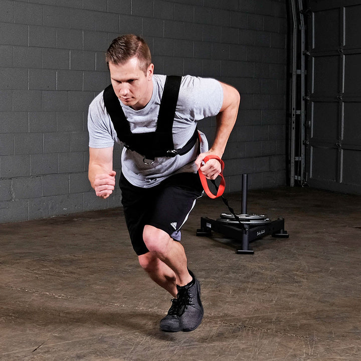 Athlete sprinting indoors while wearing the Body-Solid BSTSH sled harness for resistance training