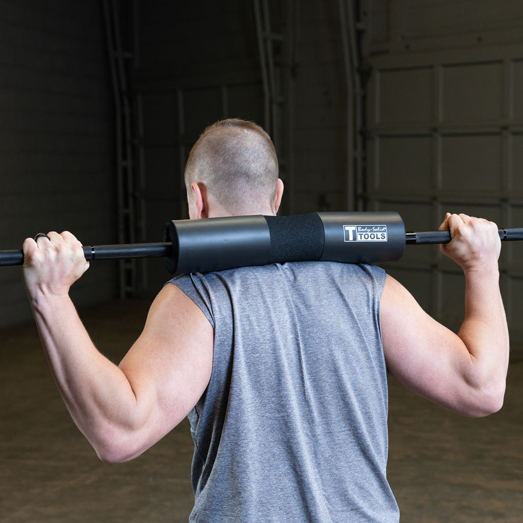 User performing barbell squats with the Body-Solid Tools premium bar pad for added shoulder comfort.