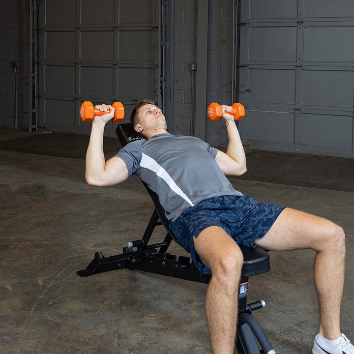 Person performing an incline press with orange Body-Solid vinyl dumbbells on a bench