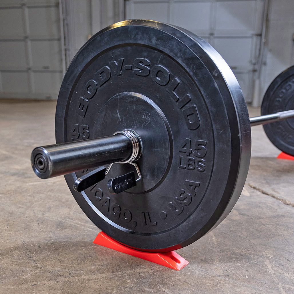 Olympic barbell resting on the Body-Solid deadlift wedge during plate changes.
