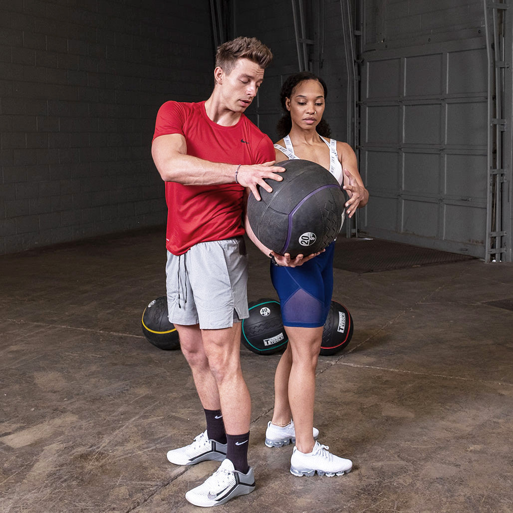 Two athletes training together using a heavy rubber medicine ball.