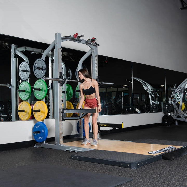 Hoist half rack in commercial gym with user lifting weights and plate storage in background