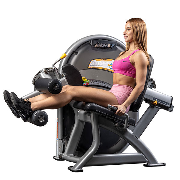 User seated on leg curl machine with legs extended and ankles positioned under rollers