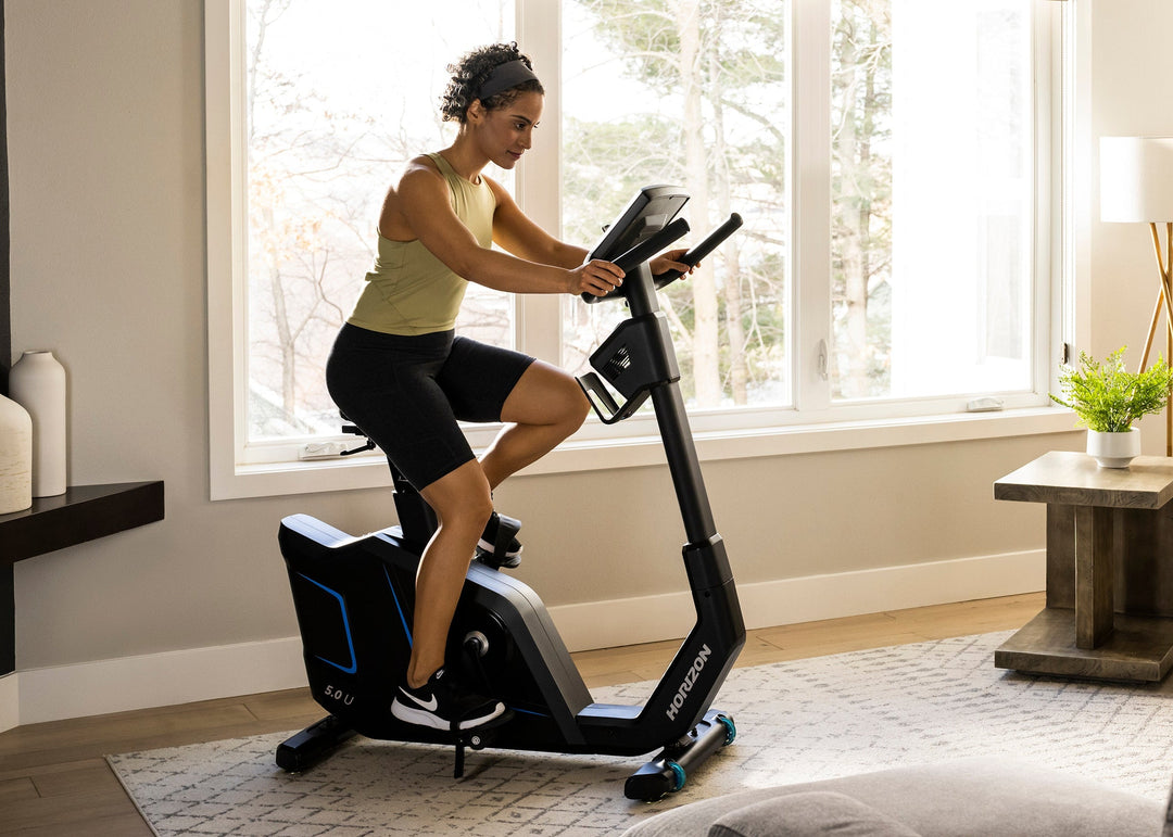 Person riding the Horizon 5.0U upright exercise bike in a home setting.