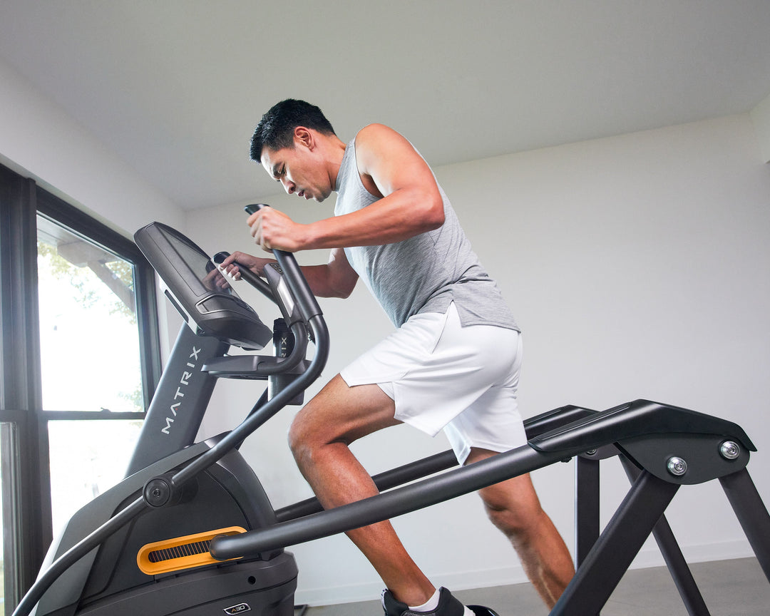 Male using Matrix A30 Ascent Trainer in mid stride with side profile view showing incline motion and full body cardio workout