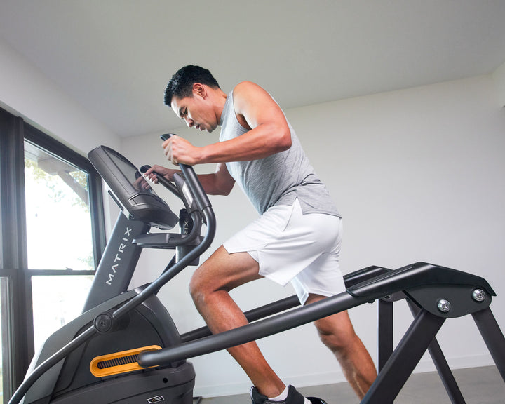 Male using Matrix A30 Ascent Trainer in mid stride with side profile view showing incline motion and full body cardio workout