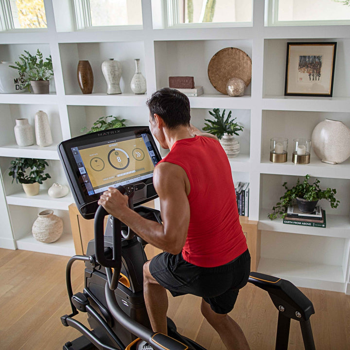 Male using Matrix Ascent Trainer in high angle back view showing incline motion and full body cardio training use