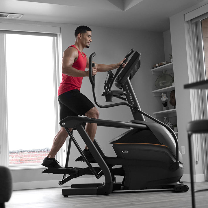 Male using Matrix elliptical in forward motion with side profile view showing smooth stride and full body cardio workout