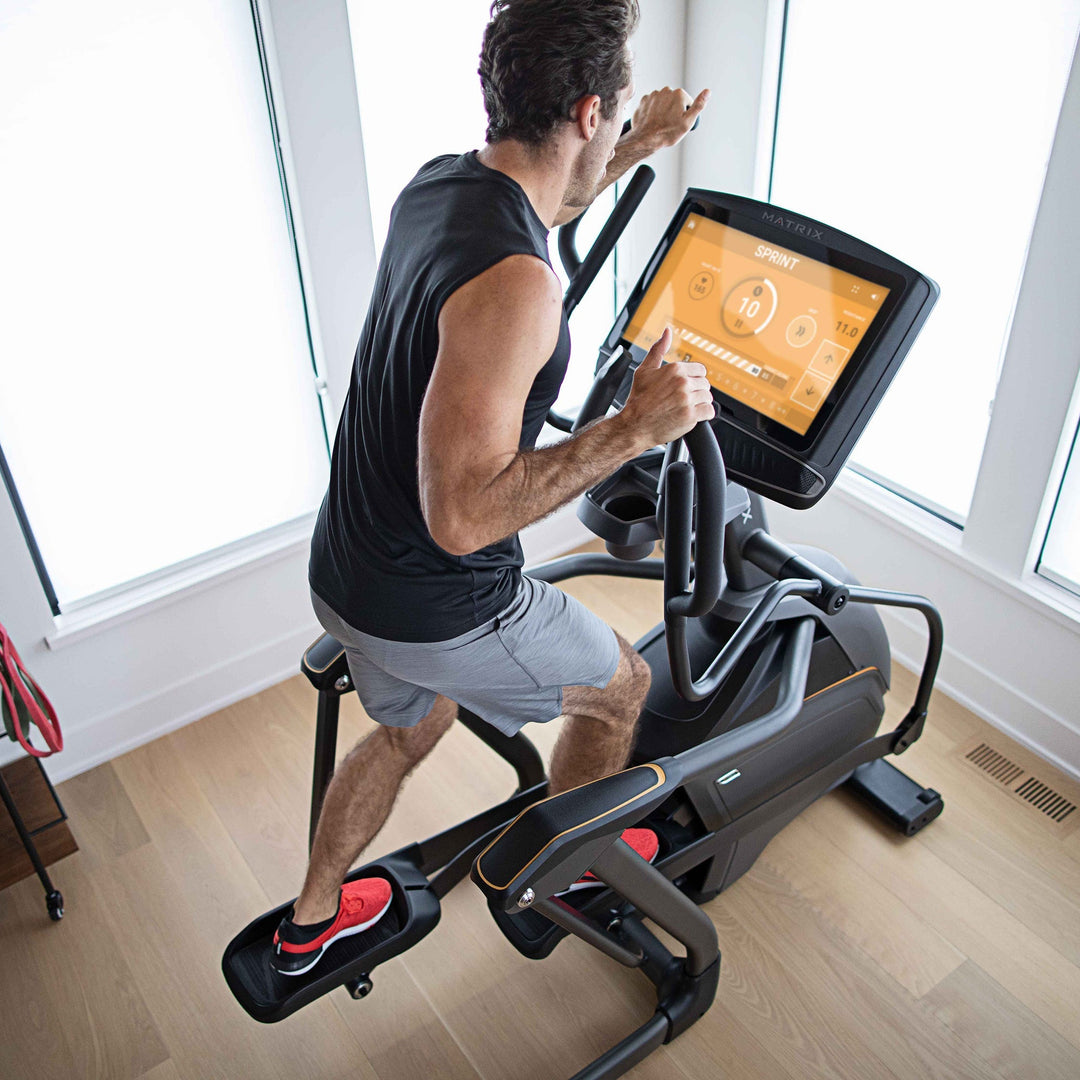 Male using Matrix elliptical in sprint workout with high angle back view showing upper body engagement and stride motion