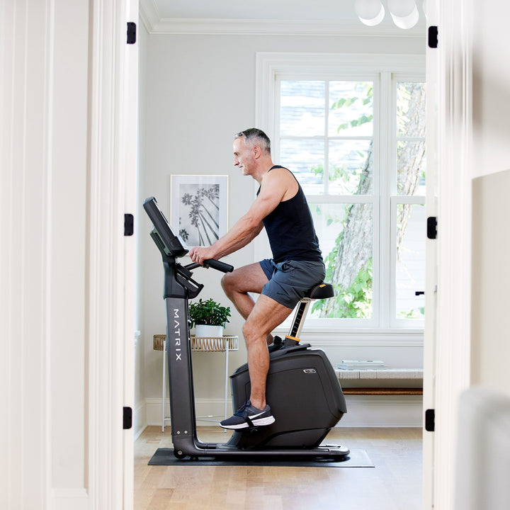 Male using Matrix U30 upright bike in side profile view showing pedaling motion and upright posture for cardio workouts