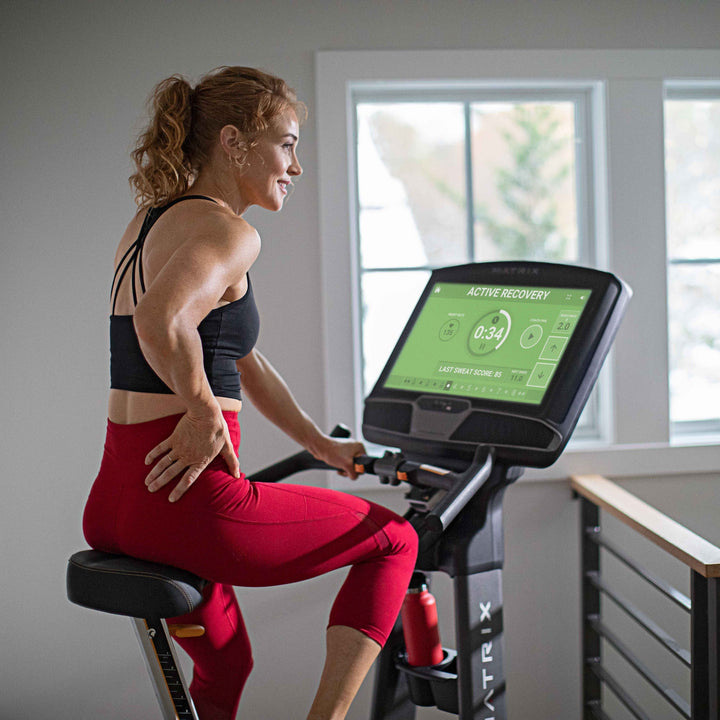Female resting on Matrix upright bike during recovery ride with back view showing relaxed posture and steady cardio use