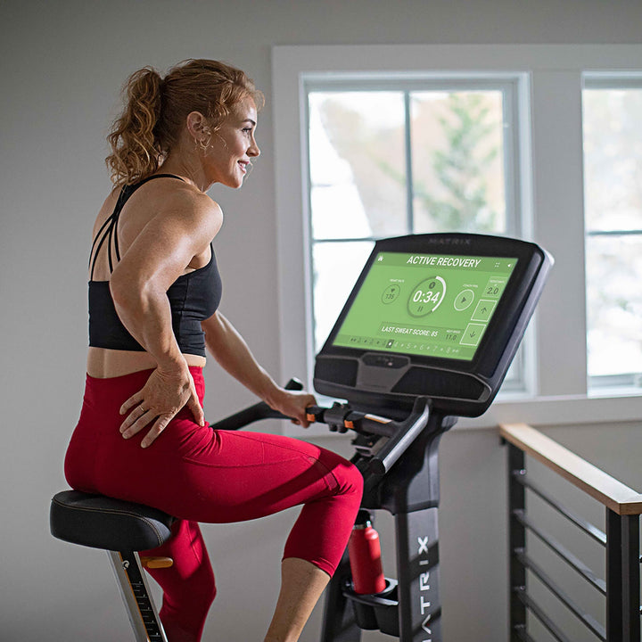 Female resting on Matrix upright bike during recovery ride with back view showing relaxed posture and steady cardio use