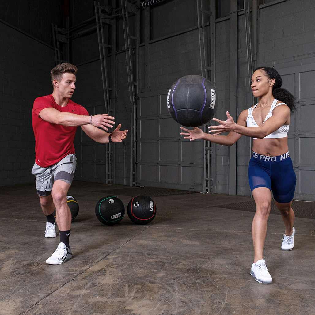 Athletes performing a partner throw using a heavy rubber medicine ball.