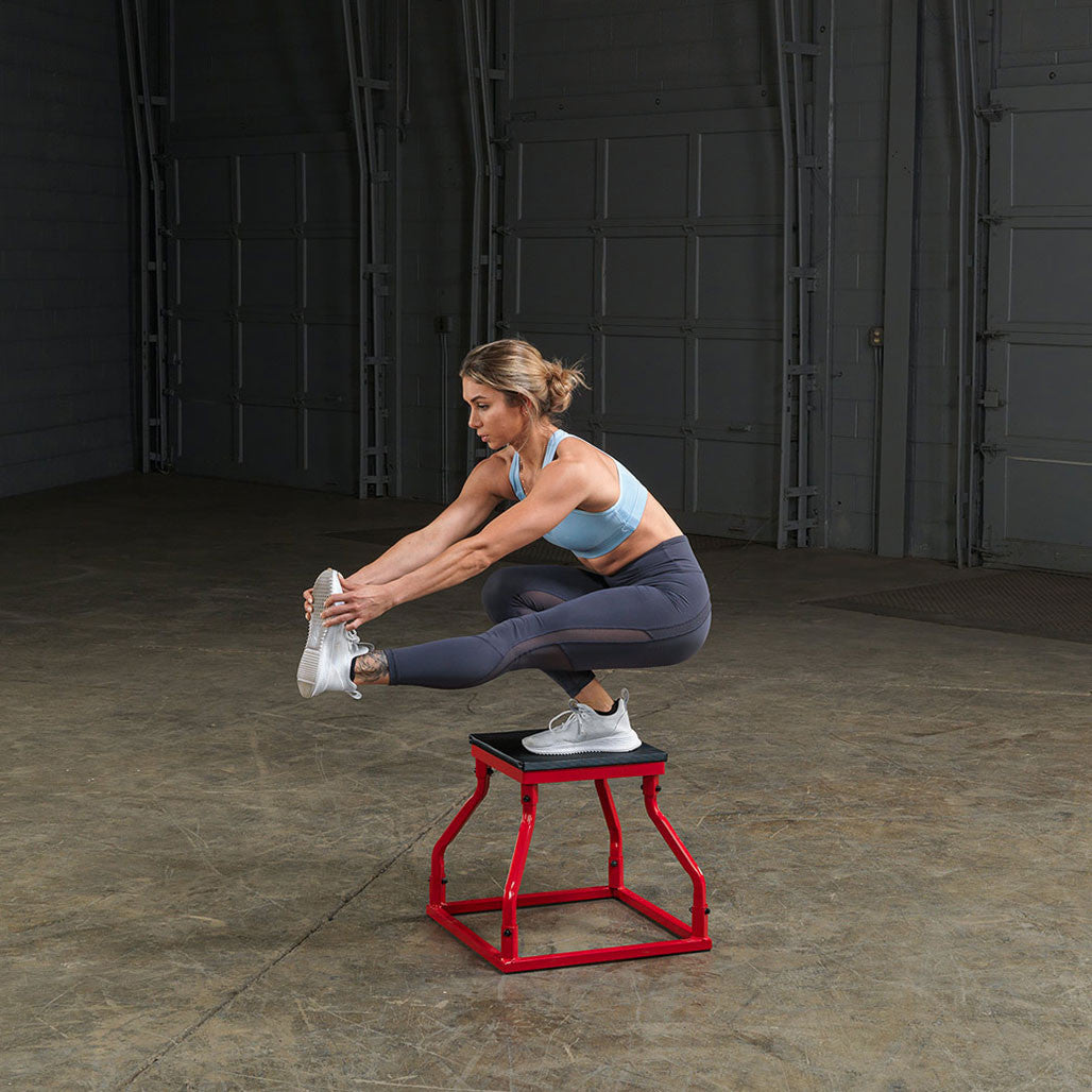 Athlete using a steel frame plyo box for seated stretching exercises.