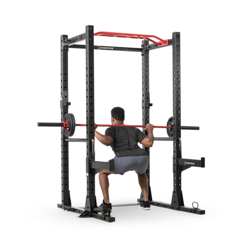 man performing barbell squats inside power cage with safety bars and rack supports