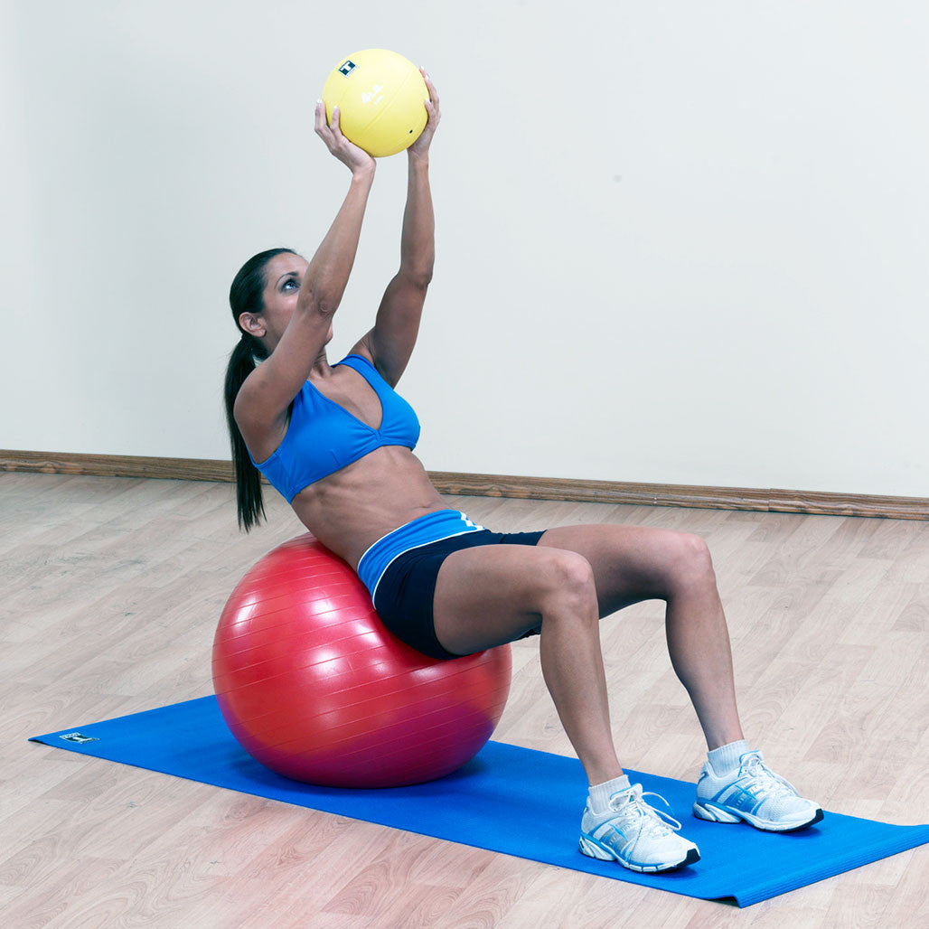 Woman seated on a red Body-Solid stability ball while performing an exercise with a small ball