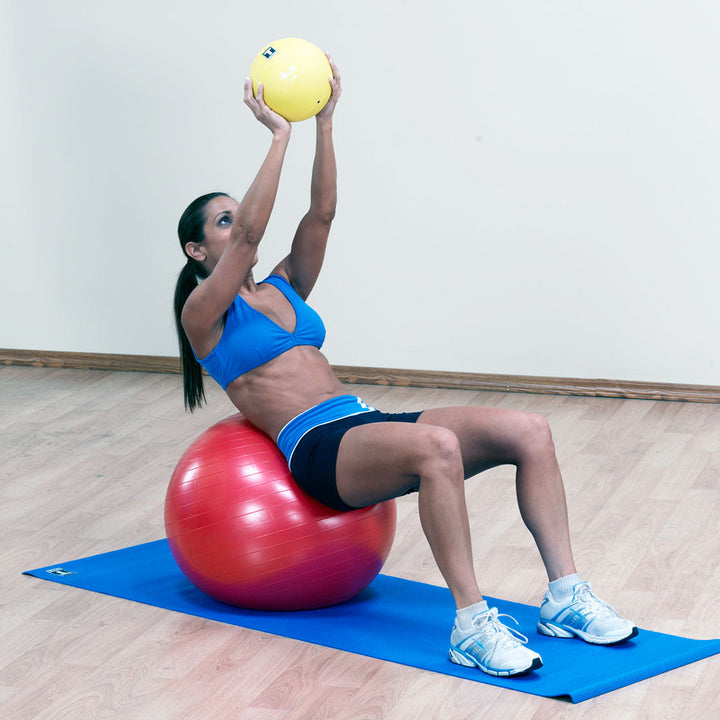 Woman seated on a red Body-Solid stability ball while performing an exercise with a small ball