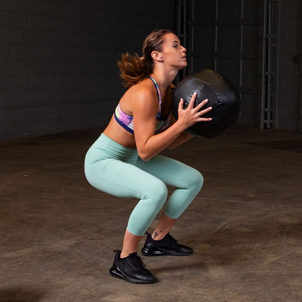 Athlete performing a squat while holding a Body-Solid soft medicine ball.