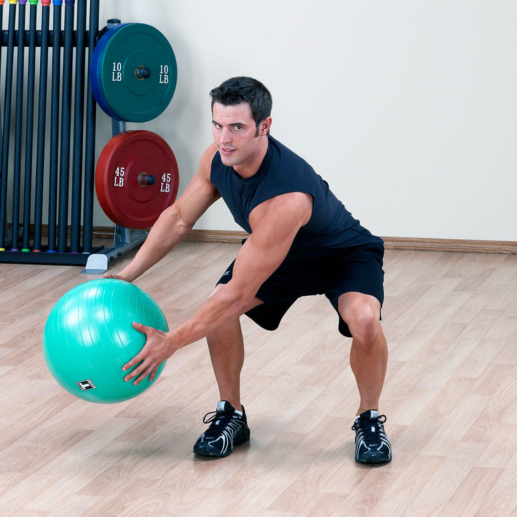 Man performing a standing training exercise while holding a Body-Solid stability ball