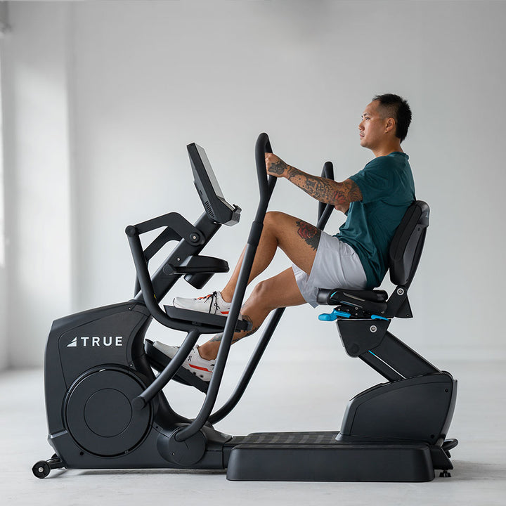 Person exercising on the TRUE Apex XRide recumbent elliptical in an indoor fitness setting