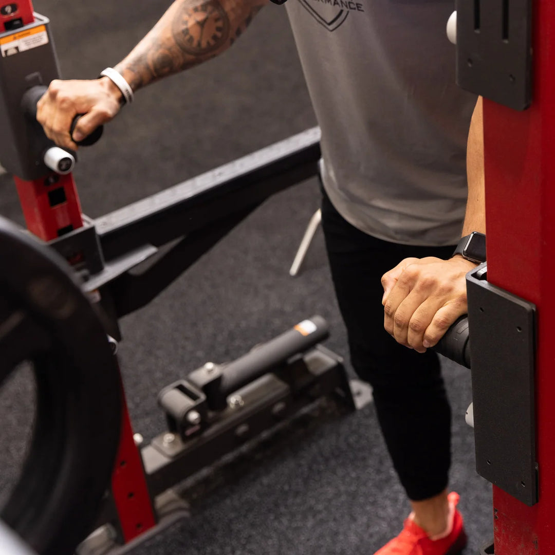 Close-up of hands gripping black Torque USA squat handle attachments during an exercise on a red gym rack.