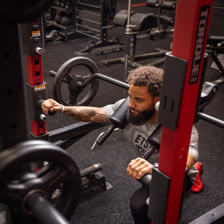 Person using black Torque USA squat handle attachments mounted on a red gym rack during a squat exercise.