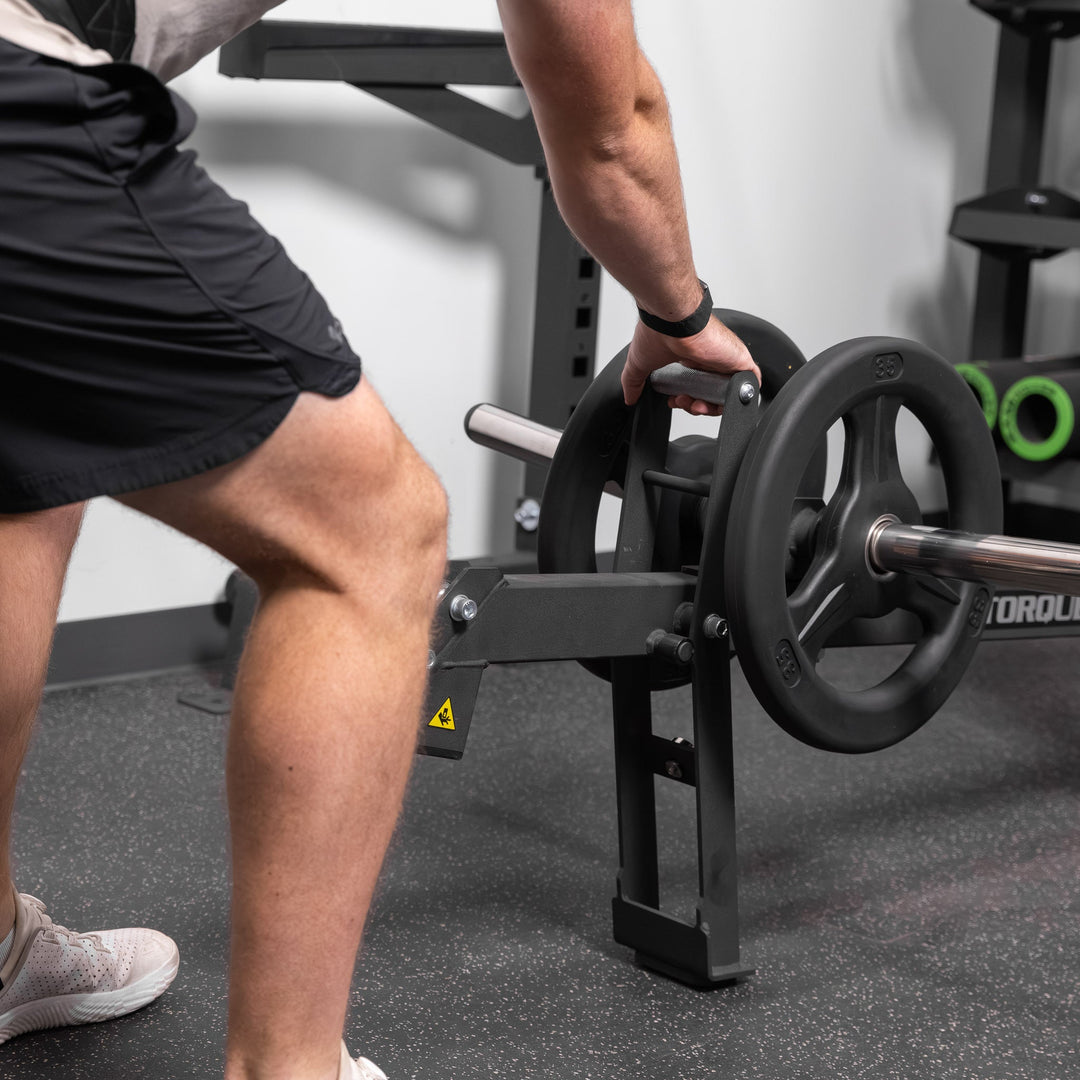 Side view of a person using the black Torque USA X-CREATE belt squat attachment with weight plates loaded.