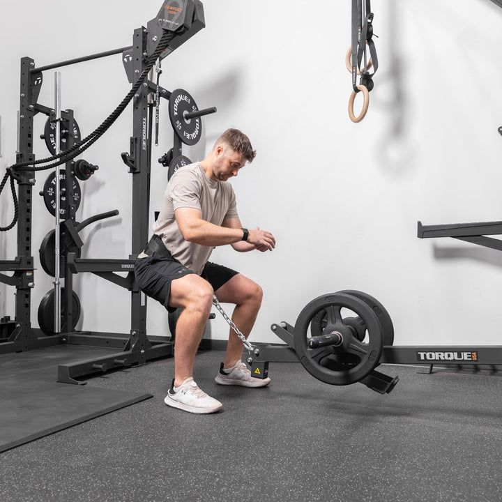 Person performing a squat with the black Torque USA X-CREATE belt squat attachment mounted on a gym training station.