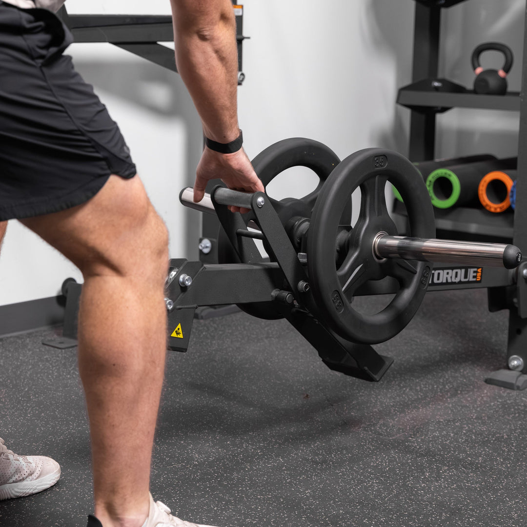 Close-up of a person using the black Torque USA X-CREATE belt squat attachment with weight plates on its loading horn.